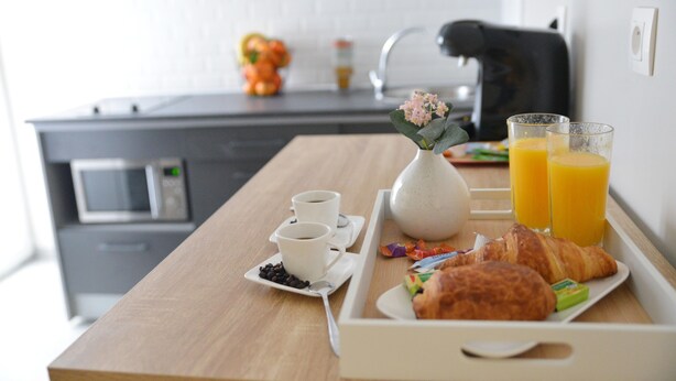 A breakfast tray with croissants, juice, coffee, and a vase of flowers on a wooden table in a modern kitchen.