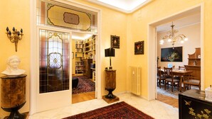 A warmly lit hallway with a large stained glass door, a wooden cabinet, a floor lamp, and a dining area with wooden furniture. - Luxury apartment next to the river (Firenze)