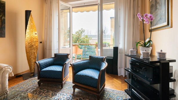 A living room with two blue armchairs, a large vase with orchids, a black entertainment unit, and a view through a glass door to an outdoor area. - Luxury apartment next to the river (Firenze)