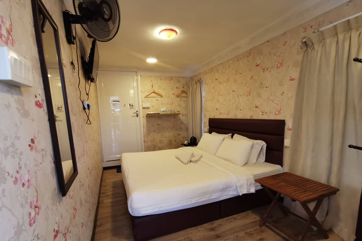 A hotel room with a bed, a wooden bench, a fan, a mirror, and a wardrobe.