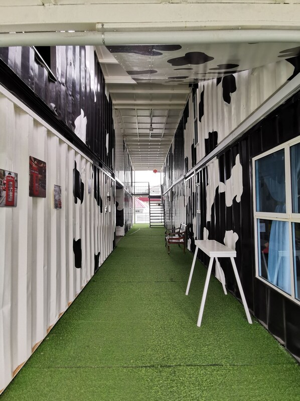 Un pasillo con césped artificial, paredes con estampado de vaca en blanco y negro, y una silla blanca.
