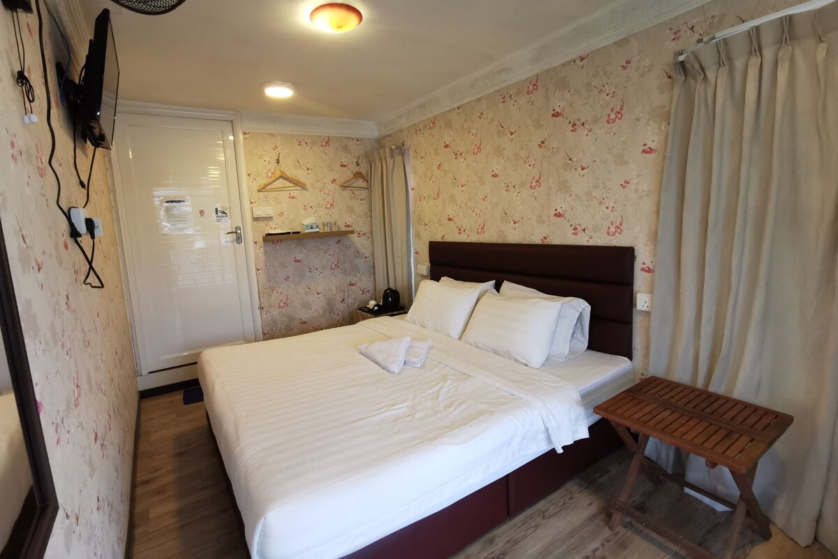 A hotel room with a large bed, a wooden bench, a ceiling fan, and a floral wallpaper.