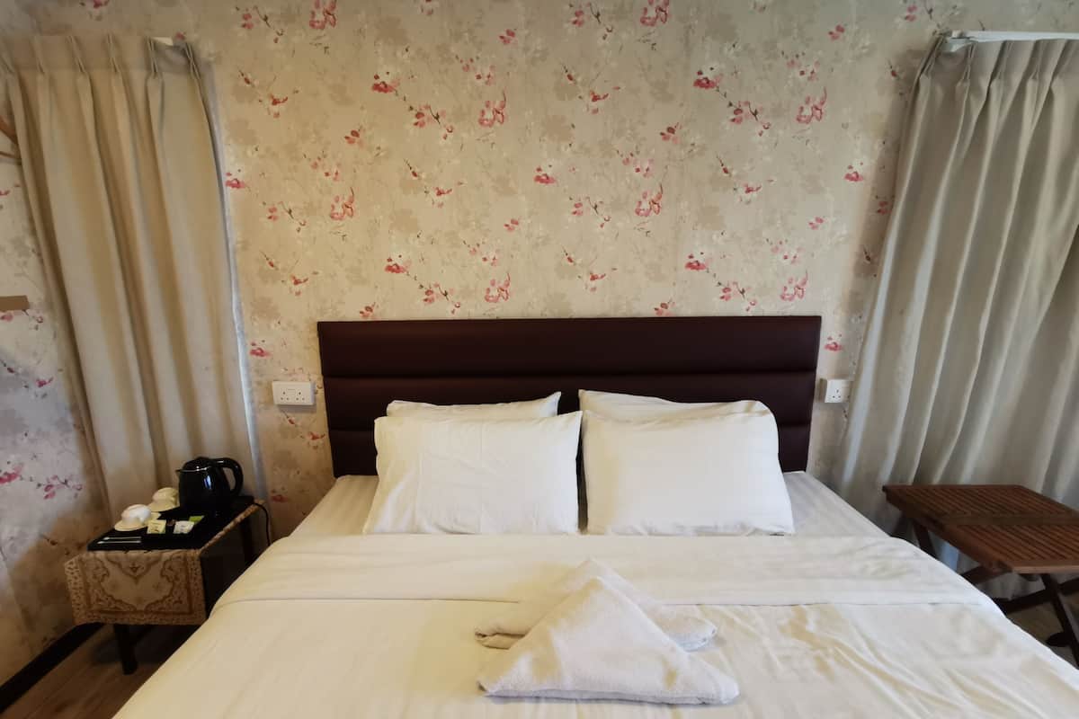 A neatly made bed with white linens and pillows, a wooden nightstand with a kettle and a small table, and floral wallpaper.