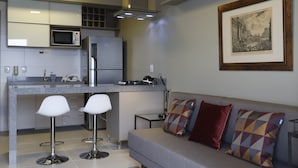 A modern kitchen with a microwave, refrigerator, and bar stools. There is a sofa with patterned cushions and a striped rug. - #1 Sophisticated Studio on Boaventura Da Silva (Fátima)