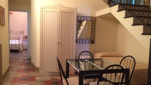 Un pasillo estrecho con una cama, un armario, una mesa de comedor con sillas y una escalera.