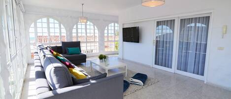Ein geräumiges Wohnzimmer mit einer großen Couch, einem Couchtisch und einem an der Wand montierten Fernseher.