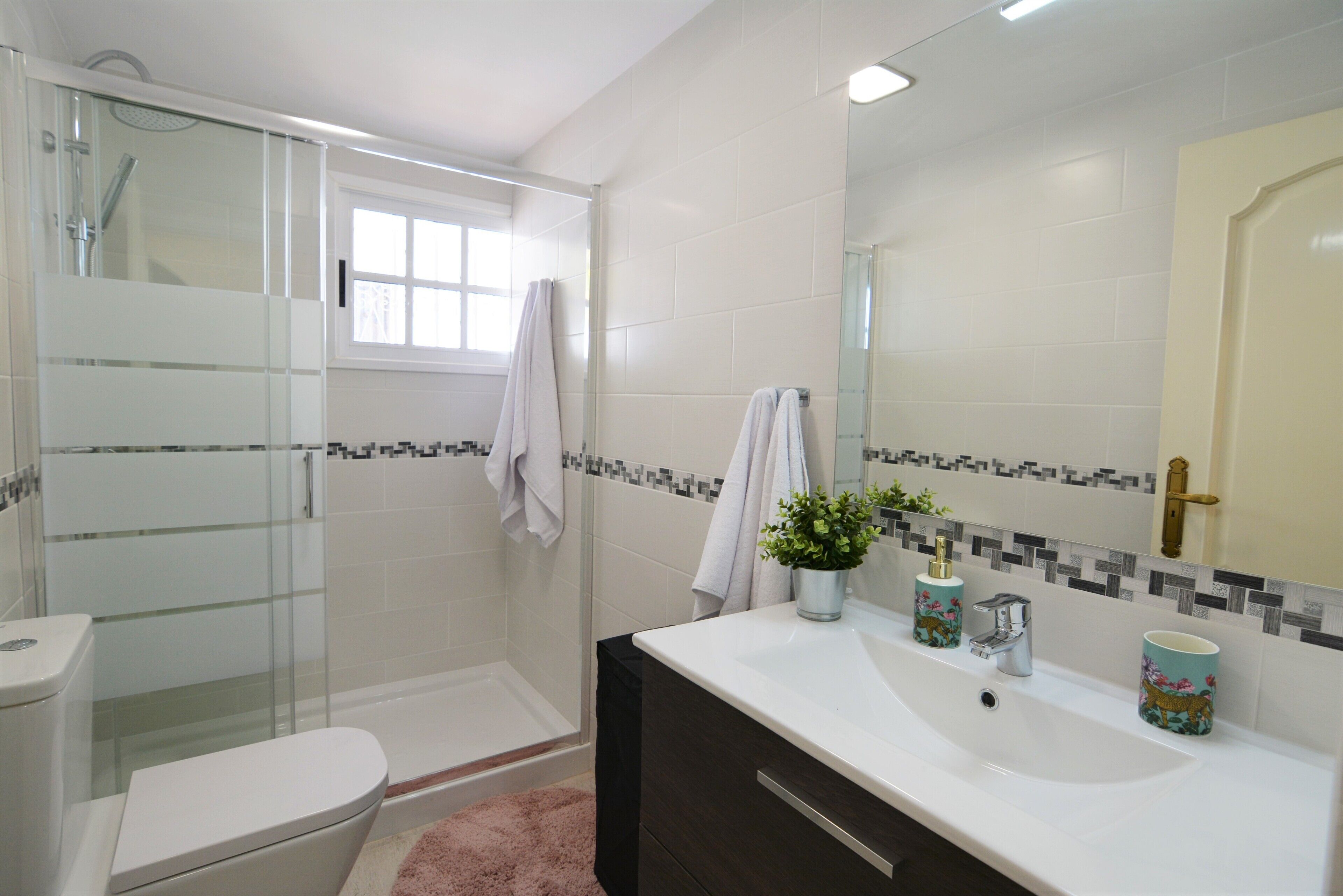 A bathroom with a glass-enclosed shower, a white toilet, a sink with decorative items, and a mirror.