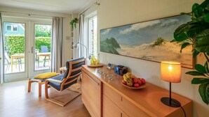 Een moderne woonkamer met een houten bureau, een comfortabele stoel, een eettafel en een groot schilderij van een strand.