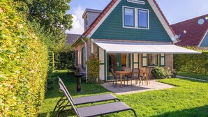 Een groene woning met een terras, een tafel en twee stoelen.