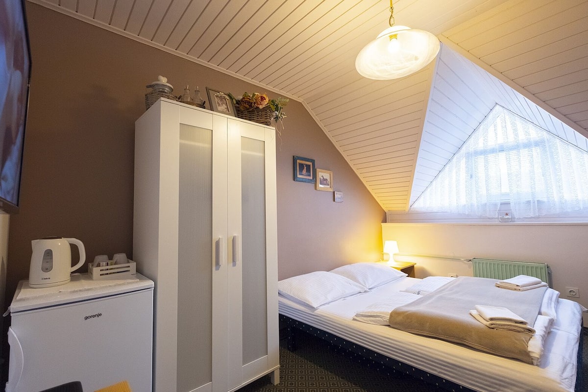 A bedroom with a bed, a wardrobe, a radiator, a window, and a ceiling fan.