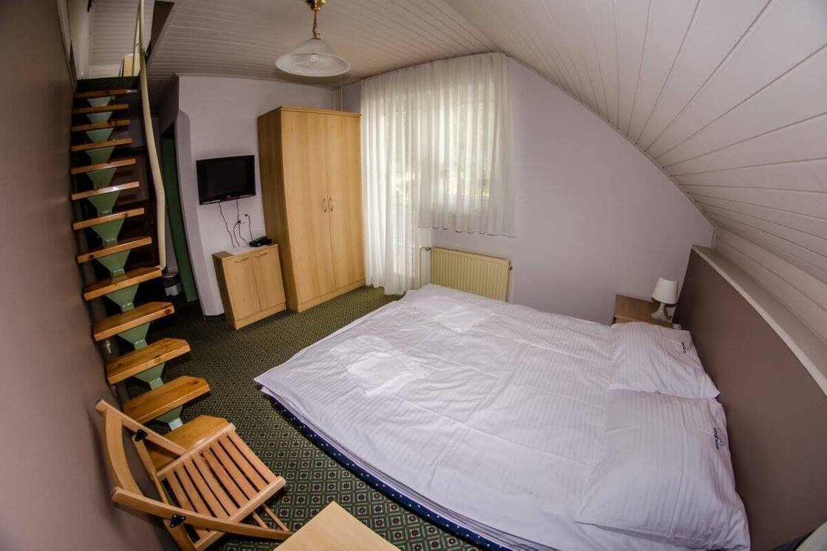 A bedroom with a bed, a wooden wardrobe, a television, a desk, and a chair.