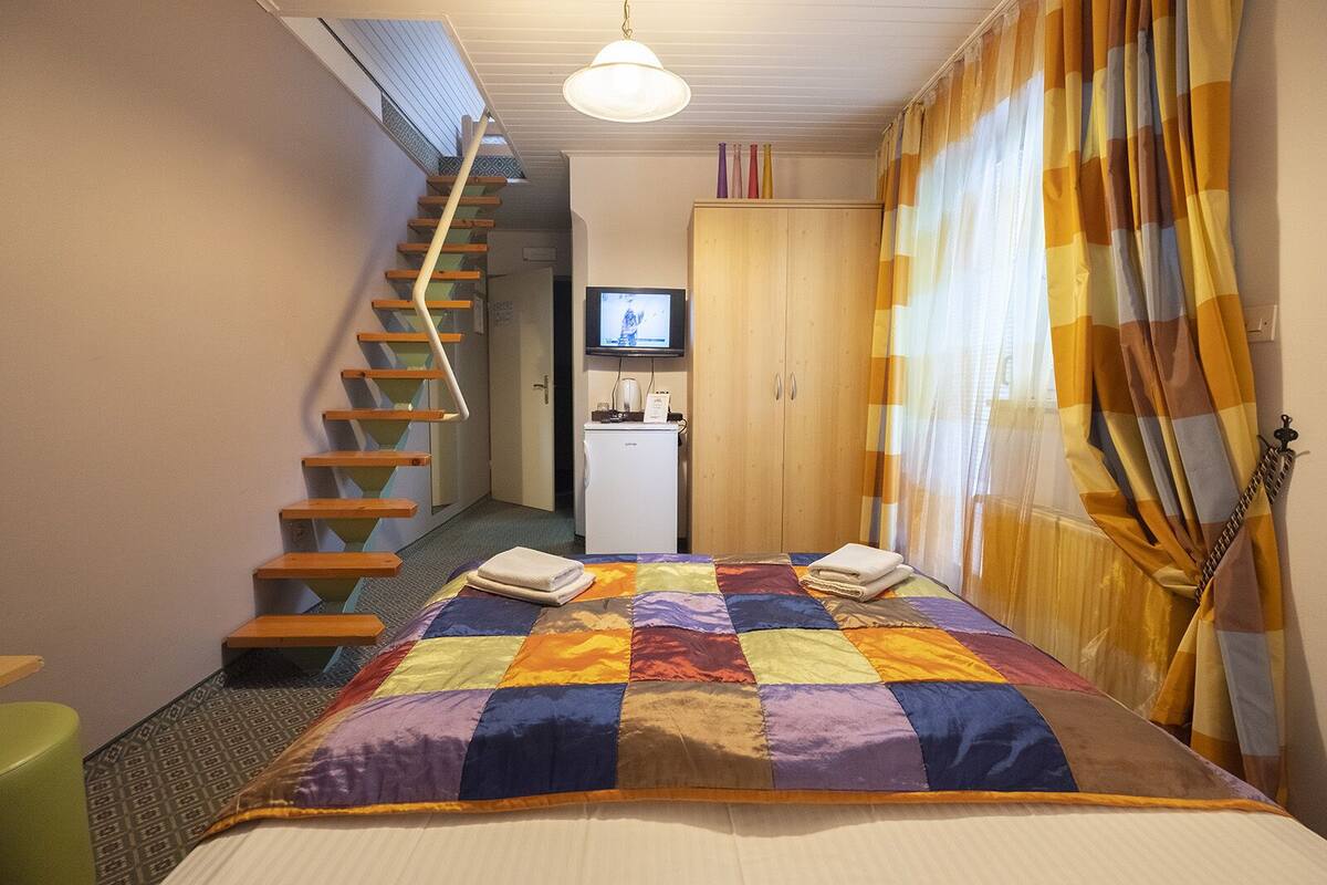 A bedroom with a bed, a wooden staircase, a television, and a wardrobe.