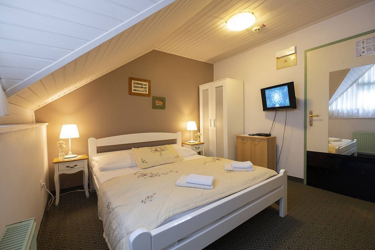 A bedroom with a bed, bedside lamps, a television, a wardrobe, and a mirror.