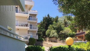 Un camino que lleva a un edificio con balcones, rodeado de follaje y un objeto esférico amarillo.