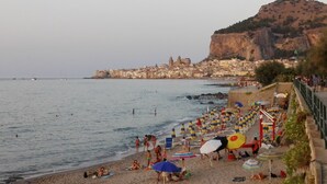 Una playa con sombrillas y gente, un acantilado rocoso y una ciudad al fondo.