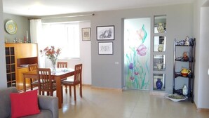 Una sala de estar con un sofá, una mesa de comedor con sillas, una estantería y un panel decorativo en la pared.