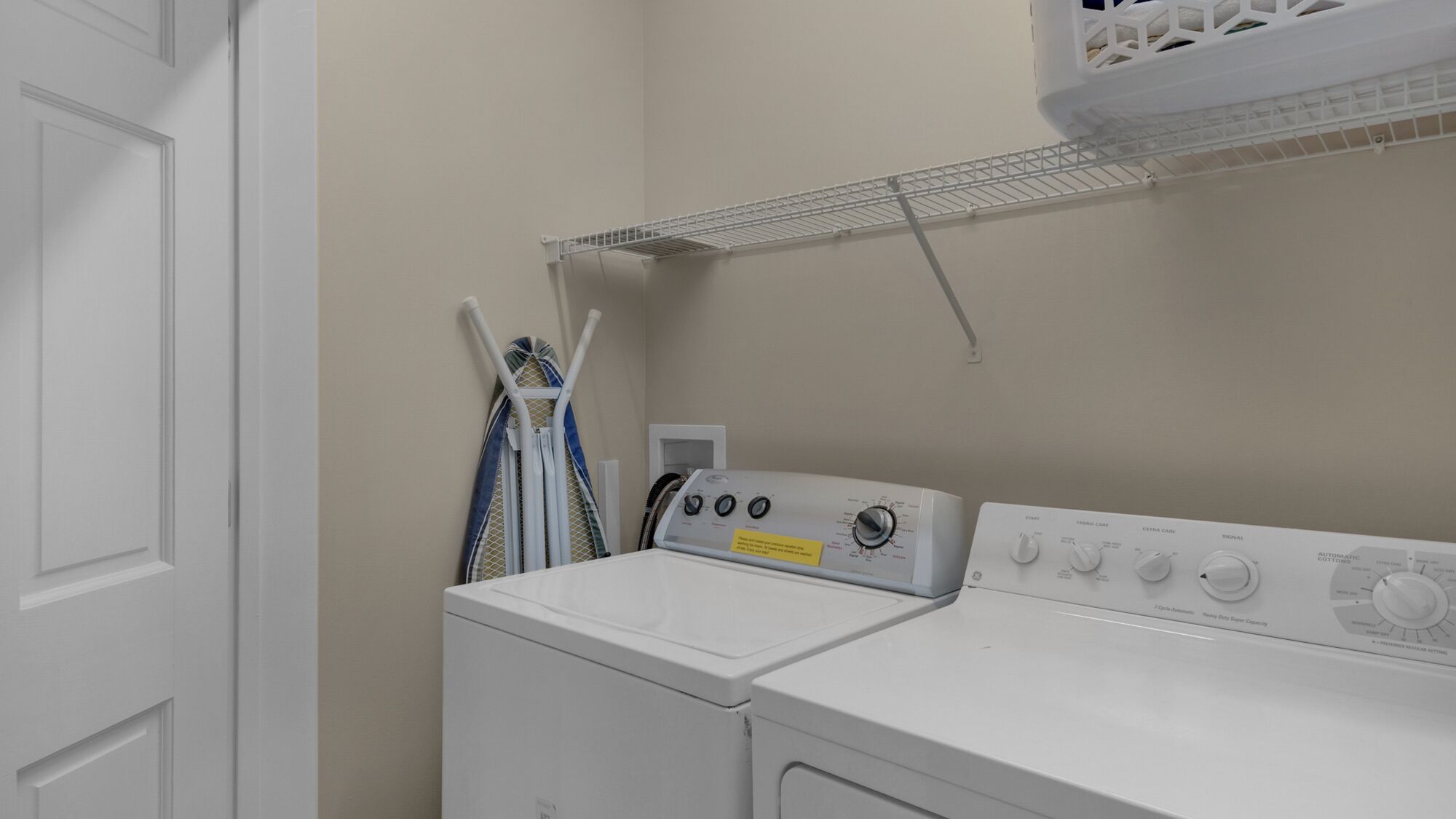 A laundry room with a front-loading washer and dryer, a metal drying rack, and a door.