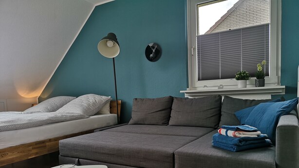 Een gezellige kamer met een grijze bank, een klein wit tafeltje en een bed met grijze beddengoed.
