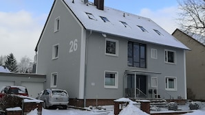 Een herenhuis met twee verdiepingen, een grijze gevel, nummer 26, met een voortuin en een zichtbare garage.