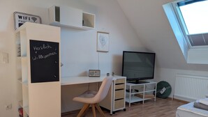 Een kamer met een bureau, stoel, televisie en raam.