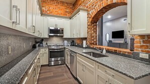 A kitchen with white cabinets, a granite countertop, a brick wall, and a stainless steel oven.