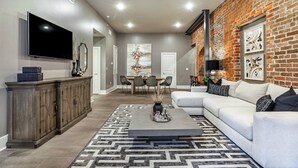 A modern living room with a sectional sofa, a flat-screen TV, a wooden cabinet, and a patterned rug.