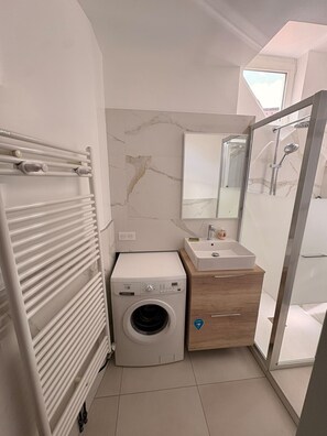Ein kleines Badezimmer mit Waschmaschine, Waschbecken und Dusche.