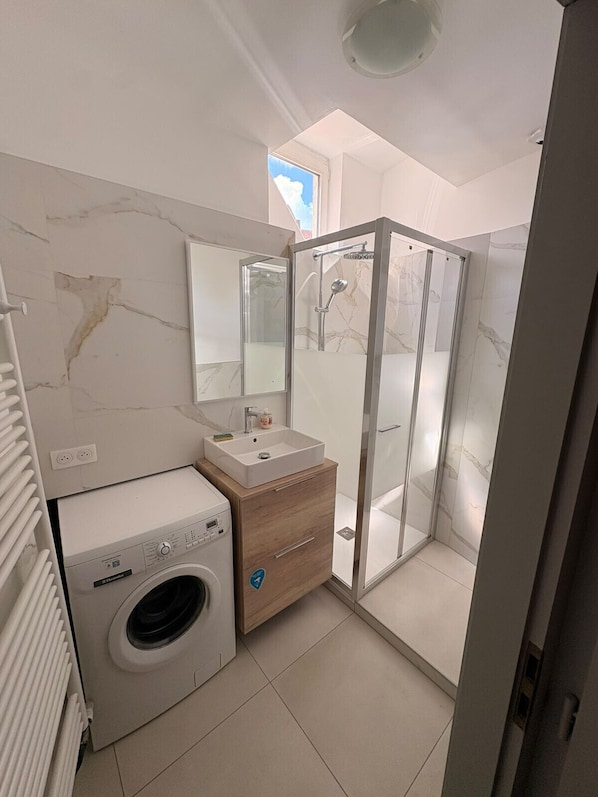 Ein modernes Badezimmer mit Duschkabine aus Glas, einer integrierten Waschmaschine und einem Waschtisch.