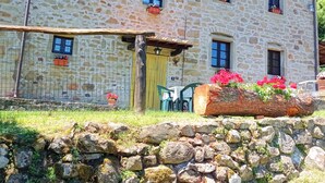 A stone building with multiple windows, some with flower boxes. There is a wooden fence and a stone wall in the foreground.