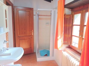 Een badkamer met een houten deur, een douche, een wastafel en een raam met gordijnen.