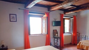 A room with a bed, a chair, a radiator, and a window with curtains.