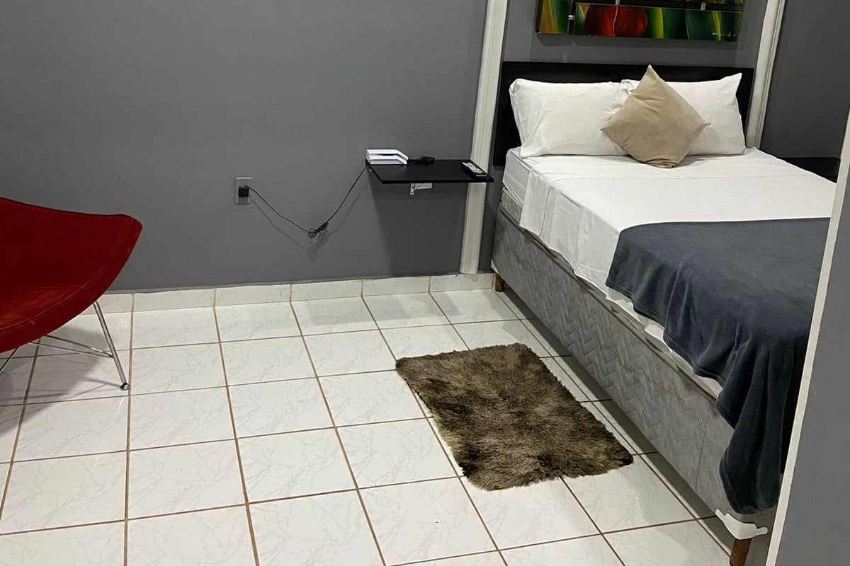Un dormitorio moderno con pared gris, un cuadro de tulipanes rojos, una cama con ropa de cama blanca y azul, una silla roja y una alfombra pequeña.