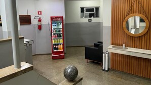 Un área de recepción con un refrigerador Coca-Cola, un espacio de descanso negro, una pared de madera con un espejo y un objeto decorativo esférico en el suelo.