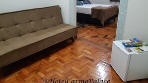 Una habitación con sofá, cama con cabecera, una mesita con objetos y suelo con diseño en espiga.