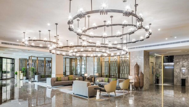 Un vestíbulo espacioso con un piso de mármol pulido, un área de estar central con sofás y sillones, y una gran lámpara de araña circular.