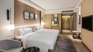 Habitación de hotel con una cama grande, un escritorio, una silla, un televisor y un baño visible a través de una puerta abierta.