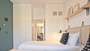 Ein Schlafzimmer mit einem großen Bett, einem Kleiderschrank, einem Nachttisch mit Lampe und einem Regal mit Bildern.