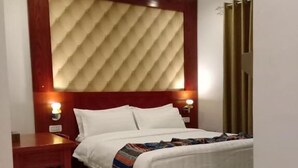 A hotel room with a bed, a wooden nightstand, a chair, and a wall-mounted headboard. - Seven Days Hotel (Aqaba)