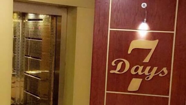 An elevator with a glass door, a wall with the number '7' and the text 'Days' in gold, and a tiled floor. - Seven Days Hotel (Aqaba)