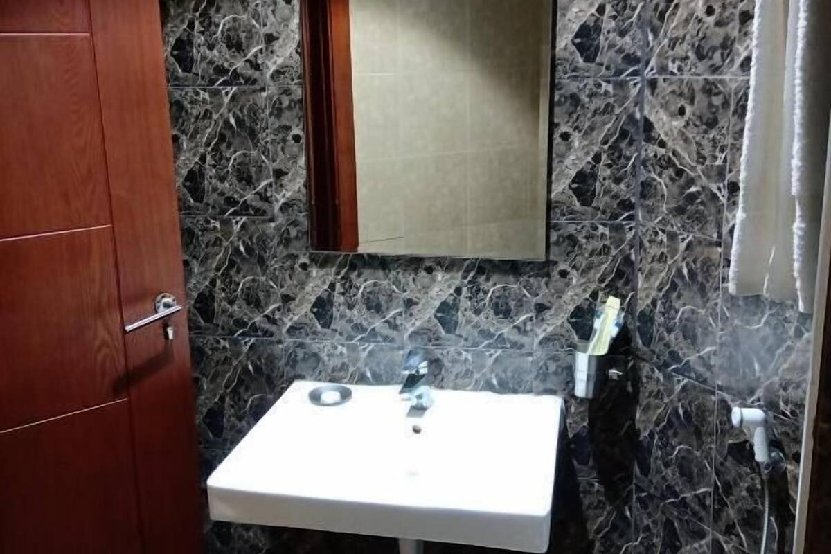 A bathroom with a marble wall, a wooden cabinet, a white sink, and a mirror.