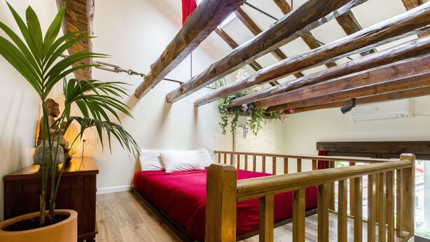 A bedroom with a wooden ceiling, a red bed, a wooden railing, and a potted plant. - Sunny n quiet penthouse in the center (Madrid)