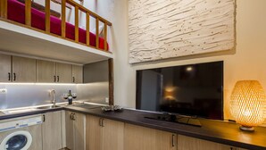 A modern kitchen with wooden cabinets, a built-in washing machine, a large flat-screen TV, and a unique textured wall art piece. - Sunny n quiet penthouse in the center (Madrid)