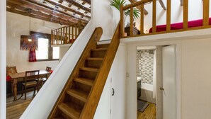 A wooden staircase leading to a balcony with a red cushion. A dining area with wooden furniture is visible below. - Sunny n quiet penthouse in the center (Madrid)