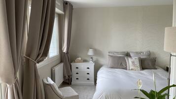A bedroom with a bed, bedside table, lamp, chair, and a plant.