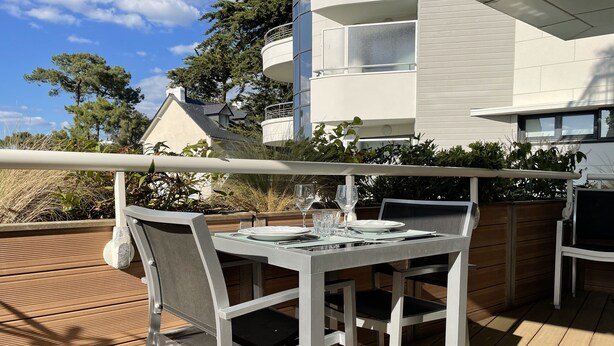 A dining area with a table set for two, outdoor seating, and a view of a modern building. - Charming 2-room terrace ideally located in a quiet area - beautiful unobstructed view. (La Baule)