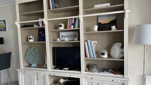 A white entertainment unit with shelves containing books, a television, and decorative items. - Charming 2-room terrace ideally located in a quiet area - beautiful unobstructed view. (La Baule)