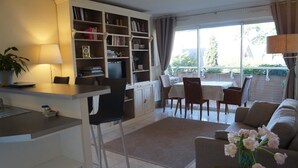 A modern living room with a dining area, a kitchen, and a large window with curtains. - Charming 2-room terrace ideally located in a quiet area - beautiful unobstructed view. (La Baule)