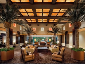 A spacious lobby with a high ceiling, large windows, and multiple palm trees.