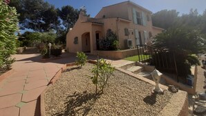 A building with a beige facade, arched entrance, and a small garden area with a pathway and gravel. - Villa large pool, beach, Sanary harbor on foot (Six-Fours-les-Plages)
