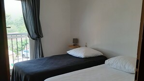 A room with two beds, a nightstand with a lamp, and a view of greenery outside. - Villa large pool, beach, Sanary harbor on foot (Six-Fours-les-Plages)